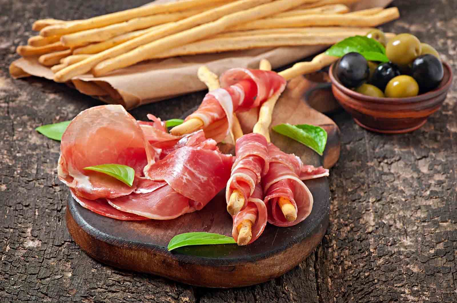 Lonchas de jamon serrano sobre tabla y palitos de pan 